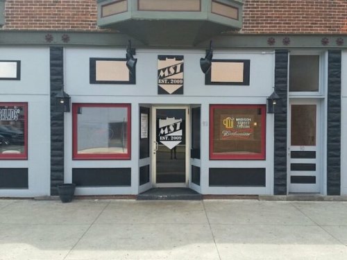 Exterior of a building featuring a sign that reads "MST EST. 2009" with red windows and a welcoming entrance.