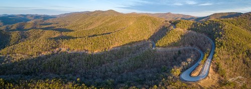 Aerial view of winding road through lush green mountains under a clear sky.