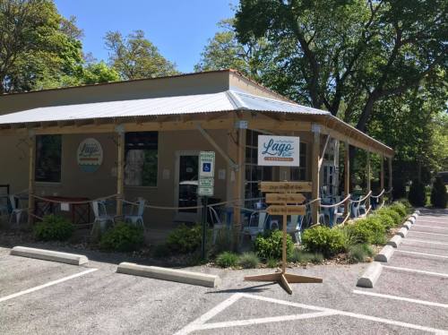 A cozy restaurant with outdoor seating, surrounded by trees and a parking lot, featuring a sign that reads "Lago."