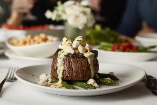 A gourmet steak topped with sauce and garnished, served on a plate with asparagus and surrounded by side dishes.