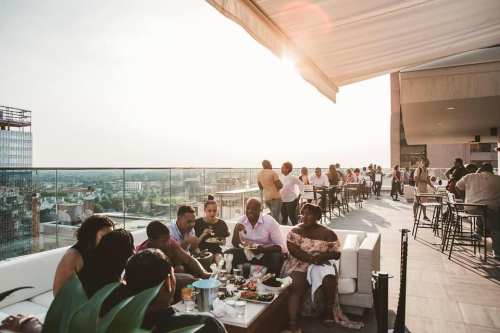 A lively rooftop gathering at sunset, with people dining and socializing against a city skyline backdrop.