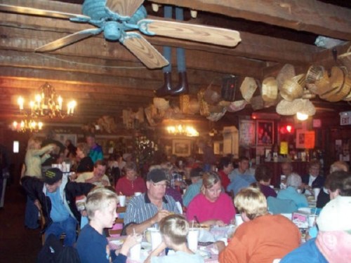 A busy restaurant interior filled with diners at tables, wooden beams, and various decorations hanging from the ceiling.