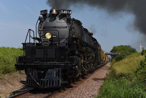 A vintage steam locomotive, numbered 4014, travels along a track with smoke billowing from its chimney.