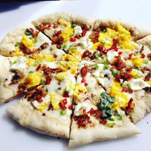 A freshly baked pizza topped with cheese, scrambled eggs, sausage, green onions, and red peppers, sliced into wedges.
