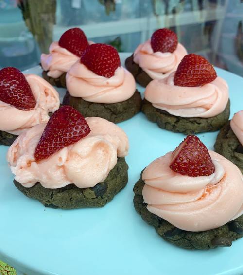 Chocolate cookies topped with pink frosting and fresh strawberries, arranged on a light blue plate.