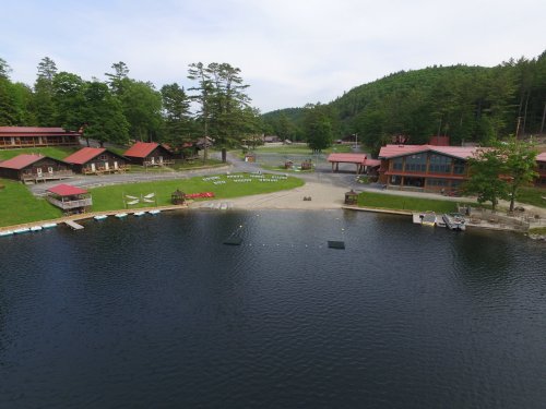 A serene lake view with cabins and a grassy area surrounded by trees and mountains in the background.
