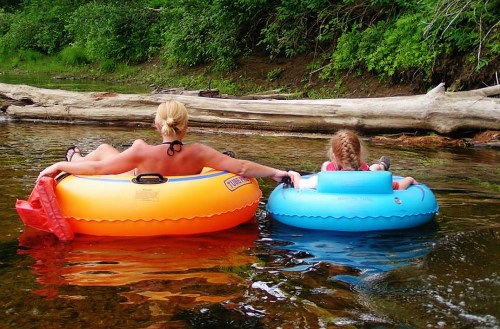 A woman and a child relax on colorful inner tubes in a calm river surrounded by greenery.