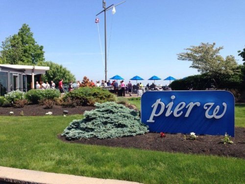 Sign for Pier W restaurant with green landscaping and blue umbrellas in the background on a sunny day.