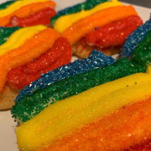 Colorful rainbow cookies topped with vibrant layers of sugar sprinkles in red, orange, yellow, green, blue, and purple.