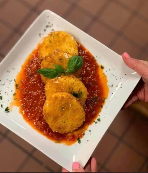 A plate of three golden fried rounds on a bed of marinara sauce, garnished with basil and herbs.