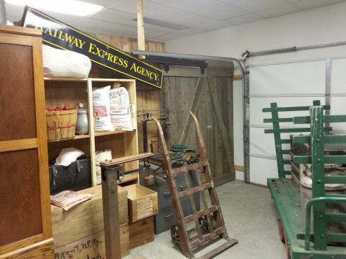 A vintage storage area featuring wooden crates, a sign for "Railway Express Agency," and old transport equipment.