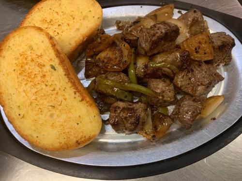 A silver platter with grilled steak pieces, sautéed onions, and green peppers, accompanied by two slices of toasted bread.
