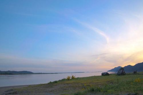 A serene river landscape at sunset, with mountains in the background and a clear blue sky.