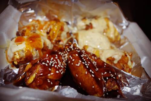 A close-up of assorted chicken wings drizzled with sauces and topped with sesame seeds, served in foil.