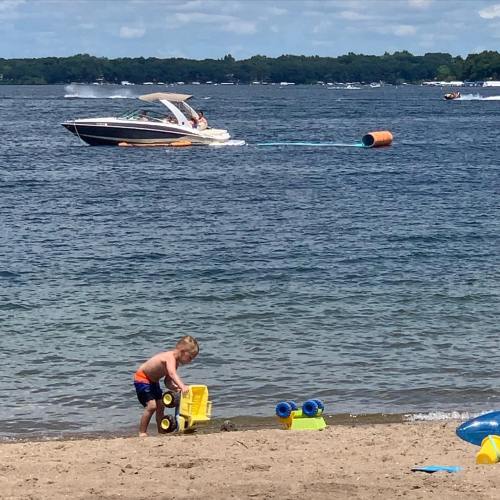 A child plays with toys on the beach while a boat speeds by on the water in the background.
