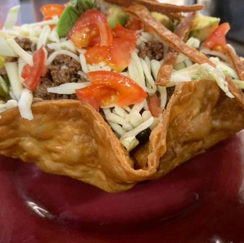 A crispy taco bowl filled with ground beef, shredded cheese, lettuce, diced tomatoes, and tortilla strips.