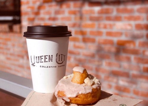 A coffee cup next to a donut topped with frosting and a small piece of cake, set against a brick background.