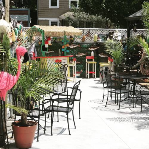 Outdoor patio with black chairs, tropical decor, and colorful accents, surrounded by greenery and a relaxed atmosphere.