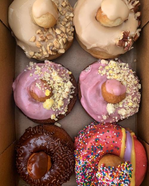 A box of assorted donuts: two glazed, two pink frosted with sprinkles, one chocolate, and one with caramel drizzle.