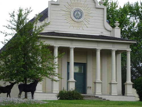 A historic building with a sun emblem, flanked by two deer statues and surrounded by greenery.