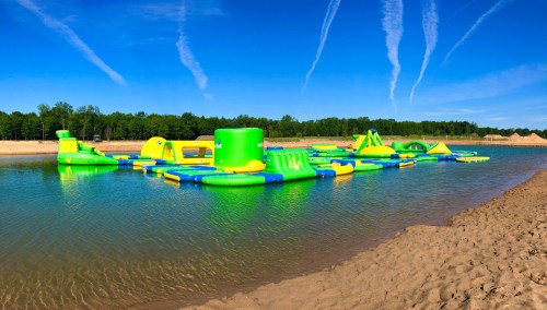 A colorful inflatable water park on a calm lake, surrounded by trees and a clear blue sky.