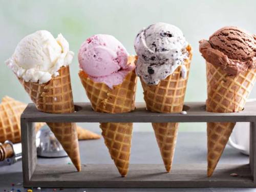 Four ice cream cones in a wooden holder: vanilla, strawberry, cookies and cream, and chocolate flavors.