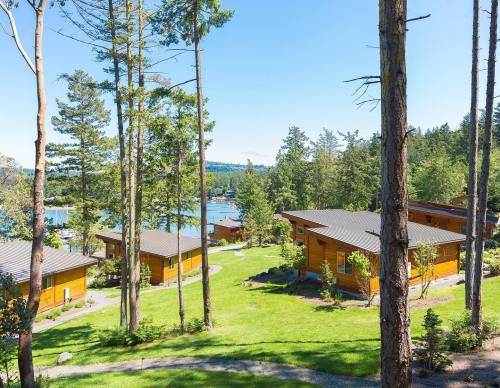 Scenic view of wooden cabins surrounded by trees, overlooking a serene lake under a clear blue sky.