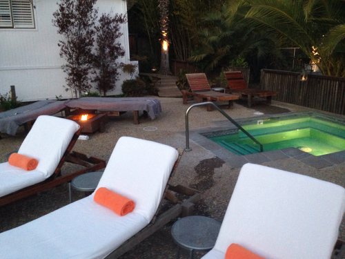 A serene outdoor space with lounge chairs, a small pool, and a fire pit surrounded by lush greenery.