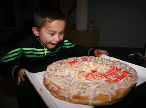 A excited child gazes at a large, decorated donut with colorful sprinkles and icing on a table.