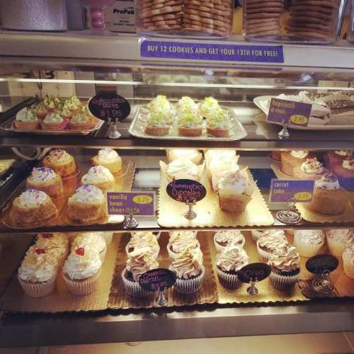 A display case filled with various cupcakes and desserts, including vanilla bean cheesecake and carrot cake.