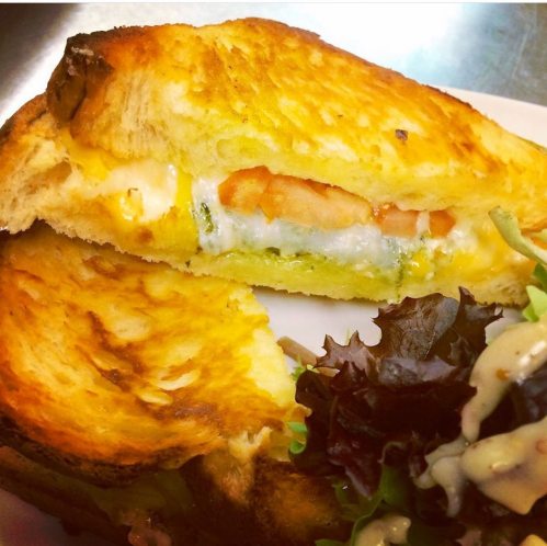 A toasted sandwich with melted cheese and shrimp, served with a side of mixed greens drizzled with dressing.