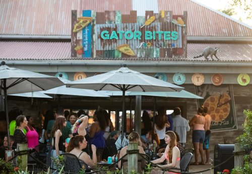 A lively outdoor dining area at Gator Bites, with people socializing under umbrellas and a rustic sign above.
