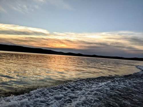 A serene sunset over a calm lake, with gentle waves and distant hills silhouetted against the colorful sky.