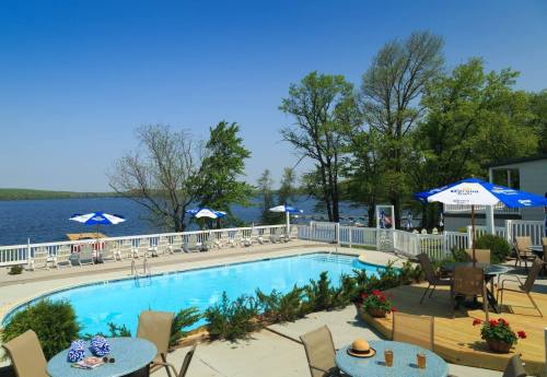 A serene poolside view with umbrellas, chairs, and a lake in the background under a clear blue sky.