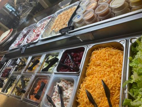 A variety of salad toppings and dressings displayed in containers, including cheese, vegetables, and sauces.