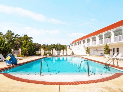 A clear blue swimming pool surrounded by lounge chairs and a white building under a sunny sky.