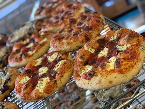 A close-up of freshly baked pizzas on a wire rack, featuring pepperoni, cheese, and herbs.