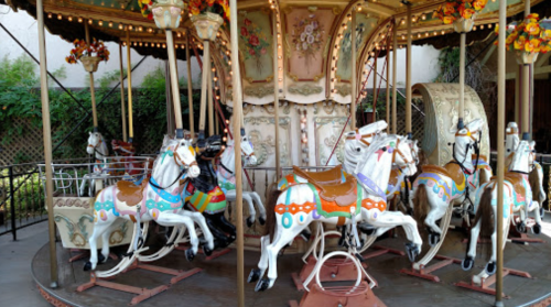 A colorful carousel with ornate horses, featuring bright decorations and a vintage design, set in a lush outdoor area.