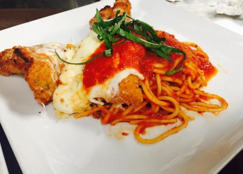 A plate of spaghetti topped with marinara sauce, mozzarella cheese, and crispy chicken, garnished with fresh basil.