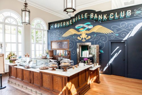 Interior of the Guerneville Bank Club, featuring a wooden counter, display cases, and a decorative mural on the wall.