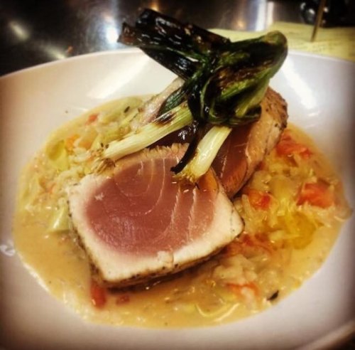 A plate of seared tuna on a bed of sautéed vegetables, topped with grilled green onions in a creamy sauce.