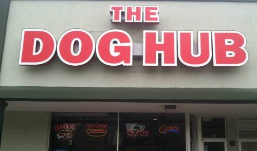 Sign for "The Dog Hub" with neon signs for burgers, hot dogs, gyros, and an "Open" indicator.