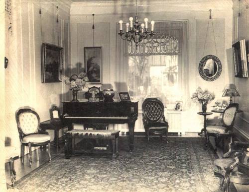 A vintage living room featuring a grand piano, elegant furniture, and decorative wall art.