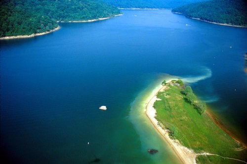 Aerial view of a serene lake with green hills, a sandy shore, and a small boat on the water.
