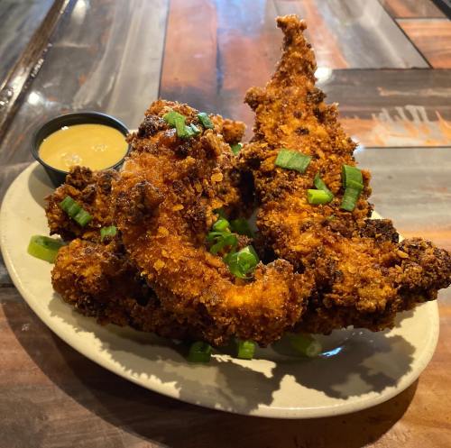 A plate of crispy fried chicken tenders garnished with green onions, served with a small cup of dipping sauce.