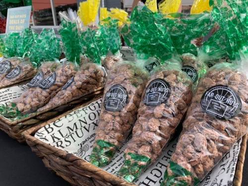 Bags of flavored nuts in green packaging displayed on a table at a market, with a sign for "Far Out Nuts."