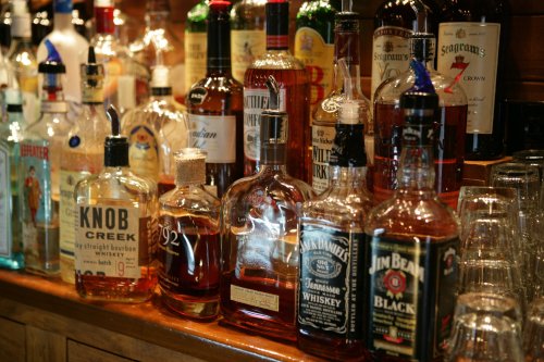A variety of whiskey and liquor bottles displayed on a wooden bar shelf.