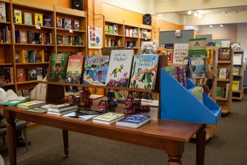 A cozy bookstore display featuring children's books on a wooden table, surrounded by shelves of colorful titles.