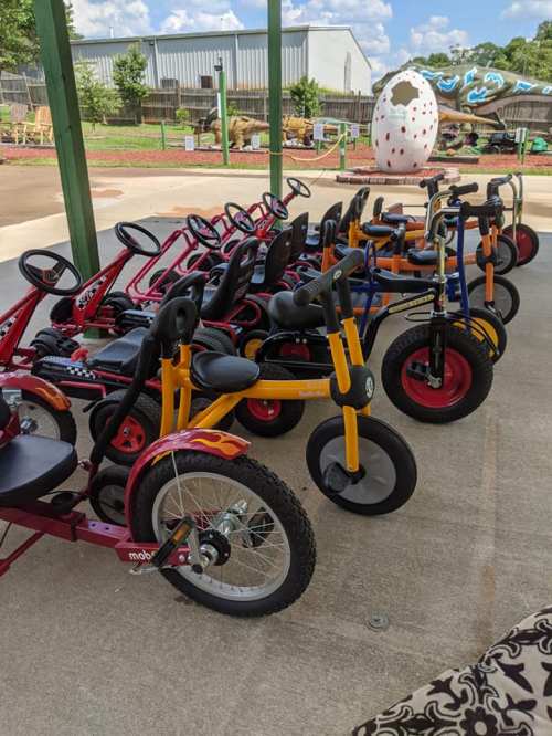 A row of colorful tricycles parked under a shelter at a playground.