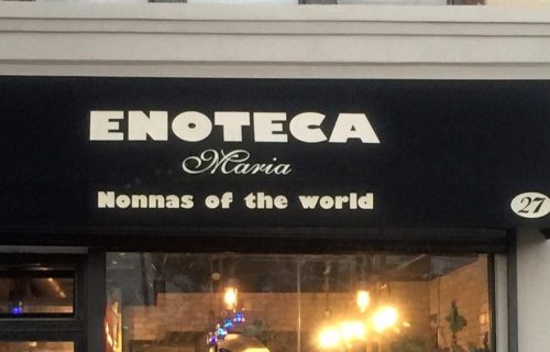 Sign for "Enoteca Maria" featuring the tagline "Nonnas of the world," with a cozy restaurant entrance.